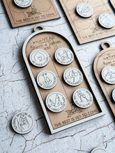 Layered Baltic birch Our Story milestone ornament with six circular coin spaces, engraved holly, the words The Best Is Yet to Come, and navy satin ribbon.