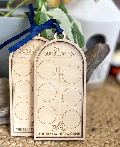 Layered Baltic birch Our Story milestone ornament with six circular coin spaces, engraved holly, the words The Best Is Yet to Come, and navy satin ribbon.