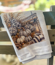 White waffle-weave tea towel printed with cream pumpkins, hydrangeas, navy chinoiserie jars, a lantern, sea oats, rope, plaid fabric, and a distant lighthouse.
