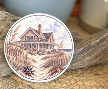 Four round ceramic coasters featuring an autumn coastal cottage, lantern with hydrangeas and shells, quiet shoreline with sea oats, and black-and-white lighthouse.

