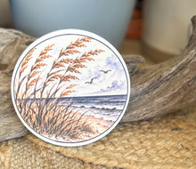 Four round ceramic coasters featuring an autumn coastal cottage, lantern with hydrangeas and shells, quiet shoreline with sea oats, and black-and-white lighthouse.
