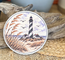 Four round ceramic coasters featuring an autumn coastal cottage, lantern with hydrangeas and shells, quiet shoreline with sea oats, and black-and-white lighthouse.
